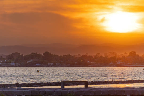 The sun is setting over the ocean, casting a warm glow over the water. The sky is filled with clouds, creating a serene and peaceful atmosphere