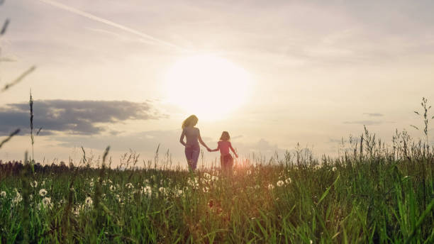 istock Mother and daughter running holding hands towards the setting sun 2162902233