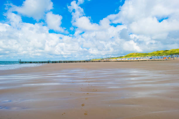 Gentle waves washing onto a sandy beach, leaving tire tracks and footprints in the sand