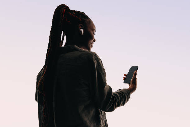 Rearview of a young woman smiling while using a smartphone app for a video chat in a studio