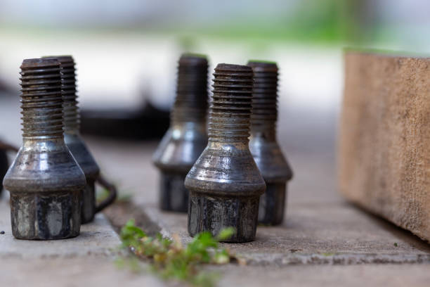 Several slightly worn bolts are scattered on the ground, removed from a car wheel