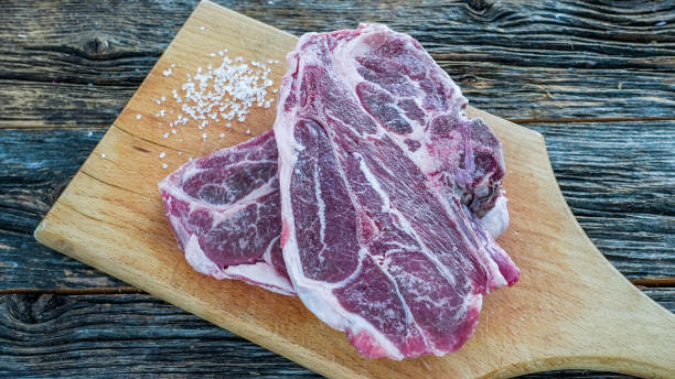 istock Two raw lamb shoulder chops are placed on a wooden cutting board, surrounded by a scattering of salt 2162909302