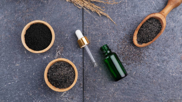 black cumin oil bottle with fresh black cumin powder on a grey surface.
