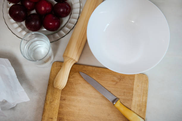 Baking preparation with bowl, rolling pin, knife, and fruit on a wooden cutting board