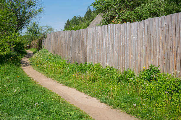 A typical street in a village with a dirt road. Path on green grass along the fence in the village, village street.