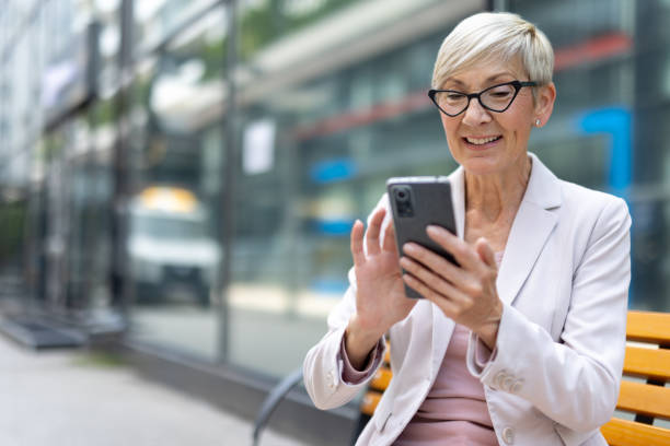 istock Senior lady browsing her phone on city bench 2162946135