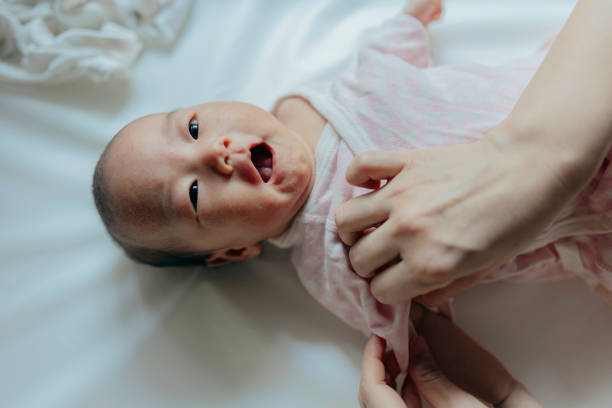 istock A baby girl is lying on the changing table while her mother is changing her clothes, performing infant care and grooming tasks. 2162960070
