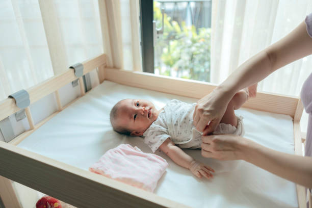 istock A baby girl is lying on the changing table while her mother is changing her clothes, performing infant care and grooming tasks. 2162960076
