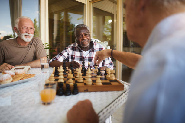 Diverse senior men playing chess in retirement home. Group of happy mature men talking while spending their time in playing chess at nursing home. friends playing chess stock pictures, royalty-free photos & images