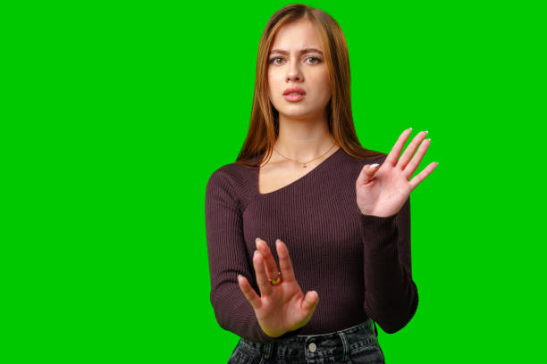 istock Young Woman With Serious Expression Holds Up Her Hand Against a Green Screen 2162966120