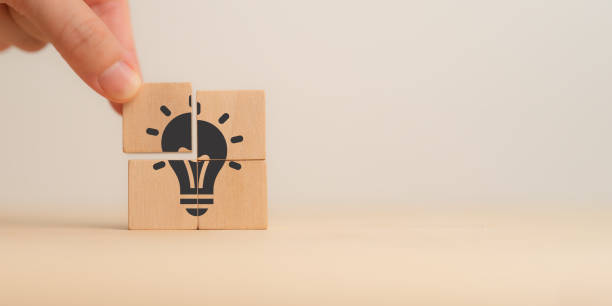 istock Ideas, creativity, innovation, problem-solving. A close-up of a hand assembling wooden puzzle pieces to form a lightbulb, symbolizing the concept of ideas, creativity, innovation and problem-solving. 2162979600