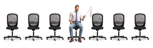 istock Sad businessman sitting between empty office chairs and holding a white flag 2162981345