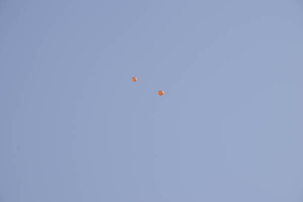 An orange helium balloon flies in the sky, released