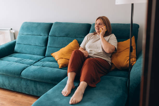 istock Happy 30s Female person talking on technology for communication. Speaking, discussion or conversation on sofa at home, happy and social media on phone call. Full body 2162982707