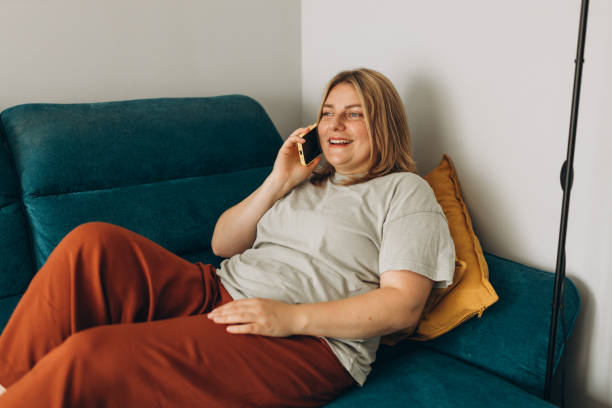 Happy 30s Female person talking on technology for communication. Speaking, discussion or conversation on sofa at home, happy and social media on phone call.