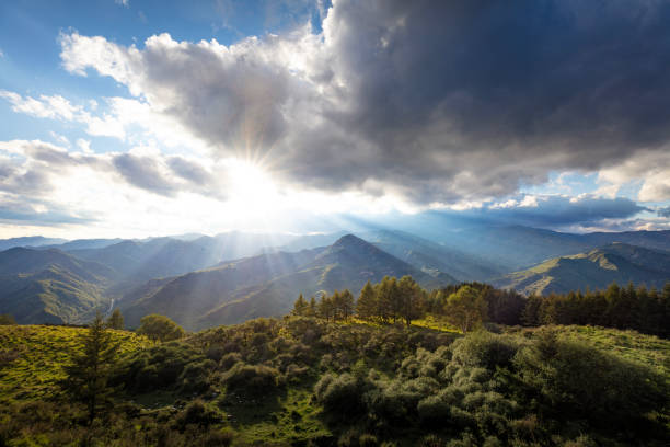 The sun shines through the clouds and hits the mountains.