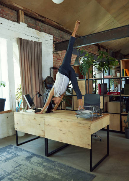 istock Athletic woman, office worker balancing yoga pose on desk while typing on computer, blending fitness and productivity in stylish loft workspace. 2162985512