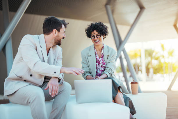 istock A businessman and a businesswoman engage in a work discussion while using a laptop on a bench outside, embodying professional teamwork in a casual setting. 2162993900