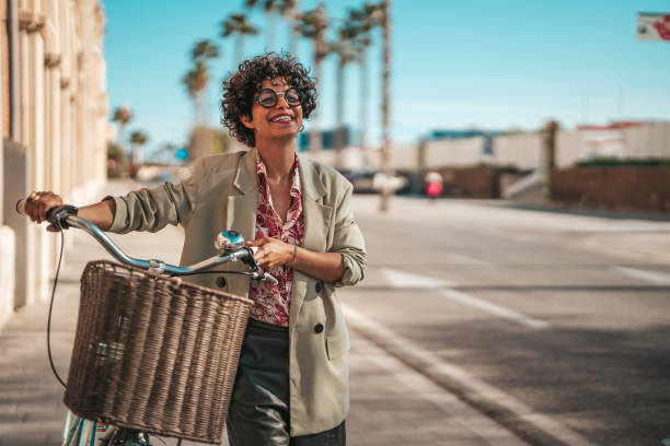 istock A Hispanic businesswoman enjoys her coffee while commuting on a bicycle, demonstrating sustainable urban travel, clad in professional attire against a city backdrop. 2162993954