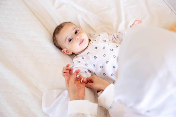 istock Smiling baby in star patterned pajamas lying on a white bed with a teddy bear, being lovingly attended by a parent. Ideal for stock photos on parenting and joy 2162995078