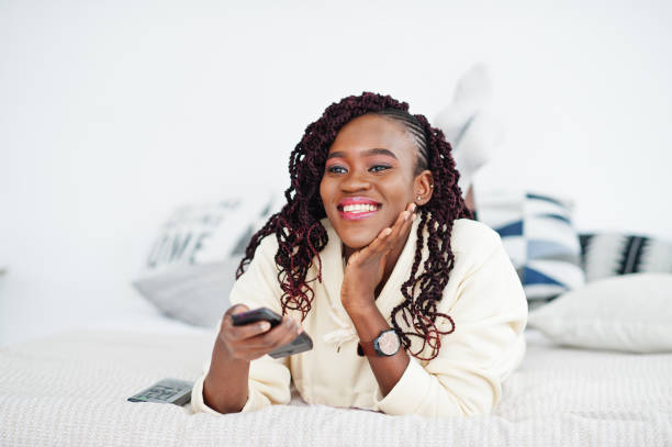 istock African woman watching tv at home and holding a remote control on bed. 2162995279