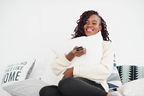 istock African woman watching tv at home and holding a remote control on bed. 2162995284