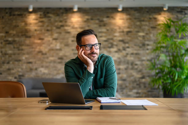 istock Contemplative entrepreneur with hand on chin looking away while working over laptop at desk in office 2162997921