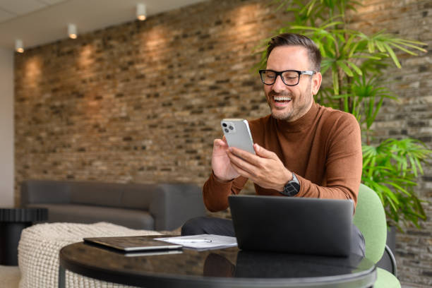 istock Young project manager reading e-mails over mobile phone while sitting with laptop at table in office 2162998078