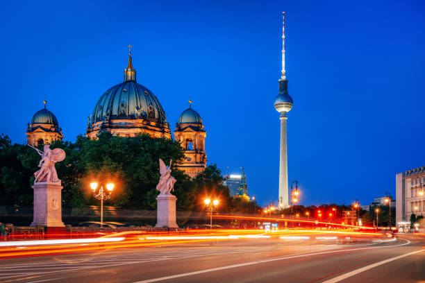 Stunning view of Berlin Cathedral and TV Tower at dusk with vibrant light trails from traffic on the street.