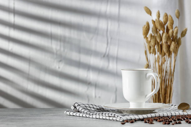 istock White cup of coffee on white table with wall with sunlight background and copy space for products. Image for montage objects display. 2163000395
