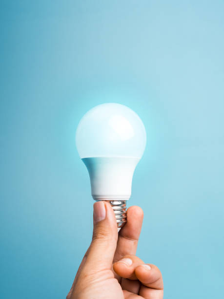 istock A White LED light bulb in hand, holding isolated on blue background, vertical style. Human finger hold environmentally friendly glowing lamp lightbulb. Creative idea, innovation technology concept. 2163000822