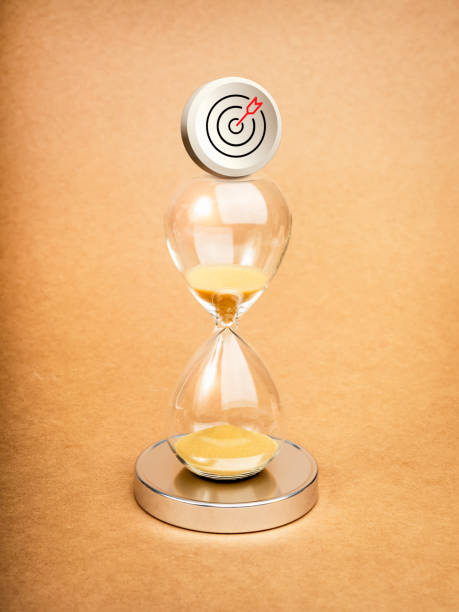 Short-term business goals encompass work that helps an organization reach its mid-term goals concept. Target dart icon badge standing on hourglass on vertical brown background, minimal style.