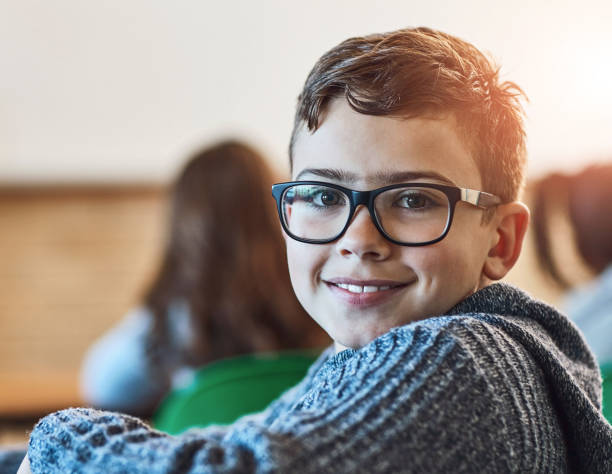 istock Boy, class and portrait of face with glasses for education, learning and development in junior school. Male learner, smile and knowledge in classroom for subject, growth and happiness for information 2163000906