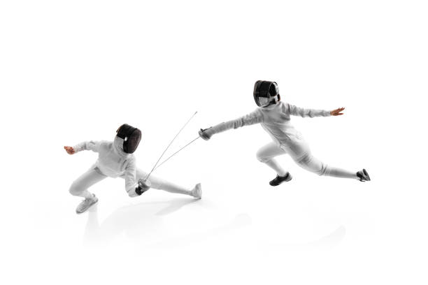 Female fencers practicing during duel, each aiming to improve their timing and accuracy against white studio background. Aerial view.