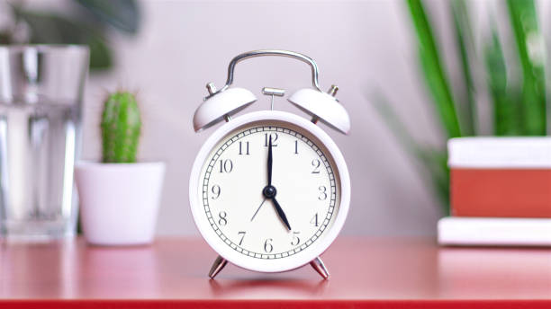 istock Classic white clock on a table. The clock hand points to 5 or 17, close up 2163010560