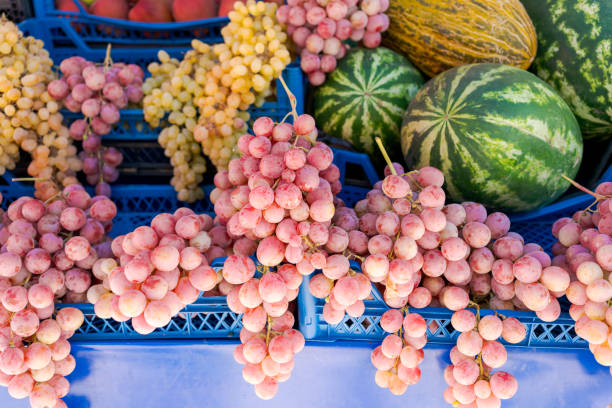 Fresh grapes of various colors and melons displayed on a blue crate at a market stand. Concept of fresh produce and healthy eating