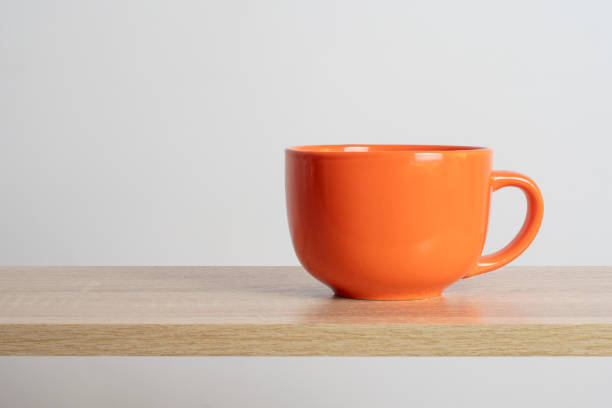 An big orange tea cup stands on a wooden surface. Light background with empty space on the theme of hot drinks.