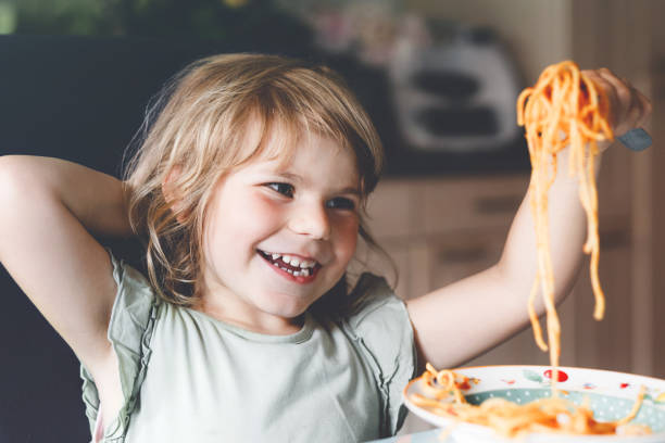Adorable toddler girl eat pasta spaghetti with tomato bolognese with minced meat. Happy preschool child eating fresh cooked healthy meal with noodles and vegetables at home, indoors. Adorable toddler girl eat pasta spaghetti with tomato bolognese with minced meat. Happy preschool child eating fresh cooked healthy meal with noodles and vegetables at home, indoors kids eating noodles stock pictures, royalty-free photos & images