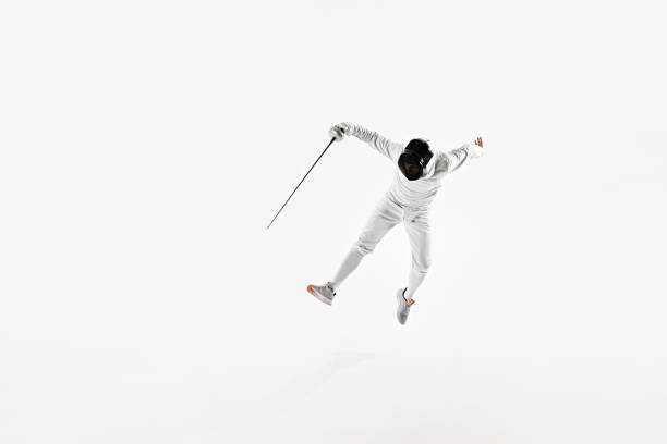 istock Fencer dressed in full white gear performing jump with their rapier pointed ahead against white studio background. 2163028732