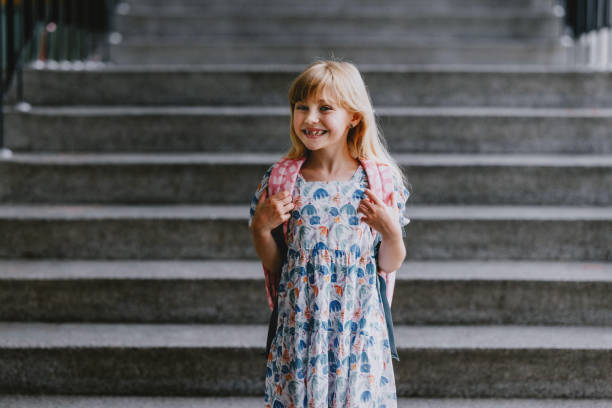 Happy young girl standing on school steps with a backpack on the first day of school. Back to school concept.