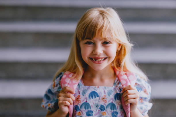 Joyful young girl standing on steps with a backpack, excited and ready for the first day of school.