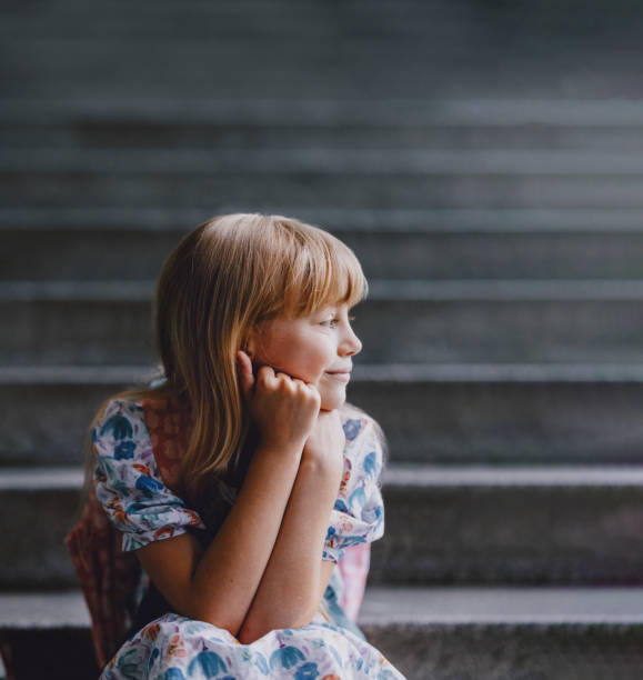 A young girl with a positive expression sitting on school steps, representing a back to school theme. Captures feelings of anticipation and happiness.