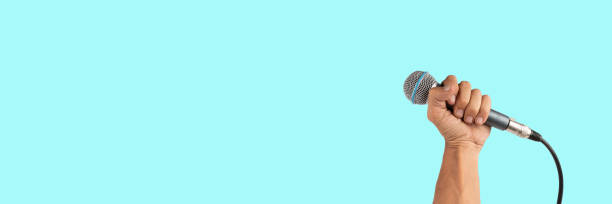 istock Black male hand holding a microphone isolated on light cyan background banner 2163041333