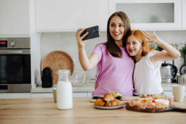 istock Mother with her daughter taking a selfie while preparing breakfast at kitchen 2163041736