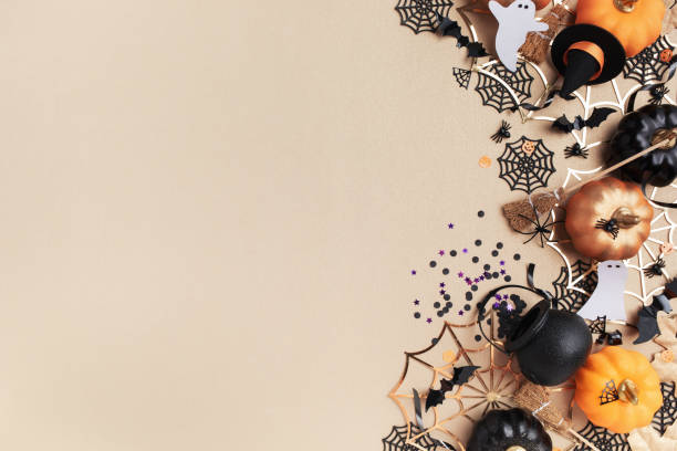 Halloween holiday frame with party decorations from pumpkins, bats, spider web and ghosts top view. Happy halloween greeting card on golden background flat lay.