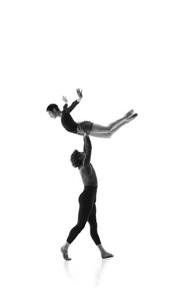 istock Elevated elegance. Young ballet dancer lifting ballerina harmonizing their moves against white studio background. Monochrome filter. 2163060493