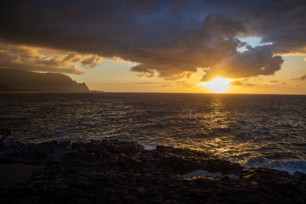 The sun sets on the rocky coastline of Kauai