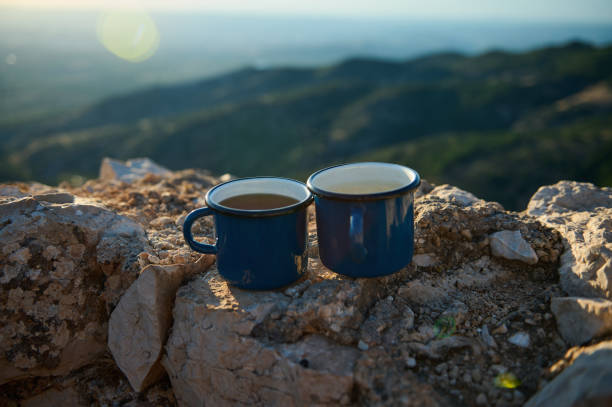 istock Two enamel mugs on a rocky surface with a scenic mountain background at sunrise 2163062948