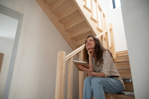 istock Woman sitting on stairs holding digital tablet thinking about home renovation 2163064458