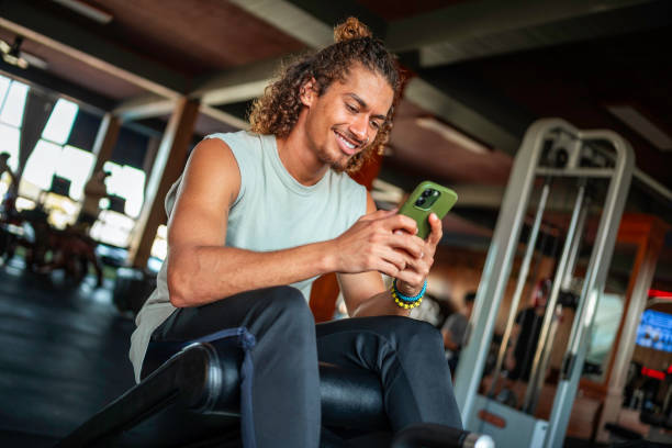 istock Smiling Hispanic Man Relaxing In Gym Using Smartphone 2163064871